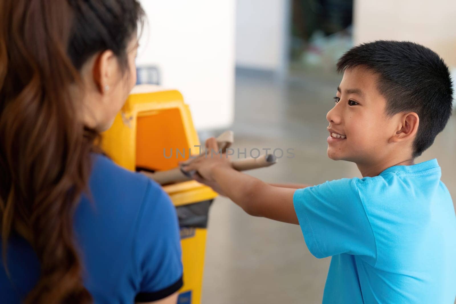 With smiles and enthusiasm, a boy and a woman engage in recycling efforts, encouraging others to join the sustainability movement.