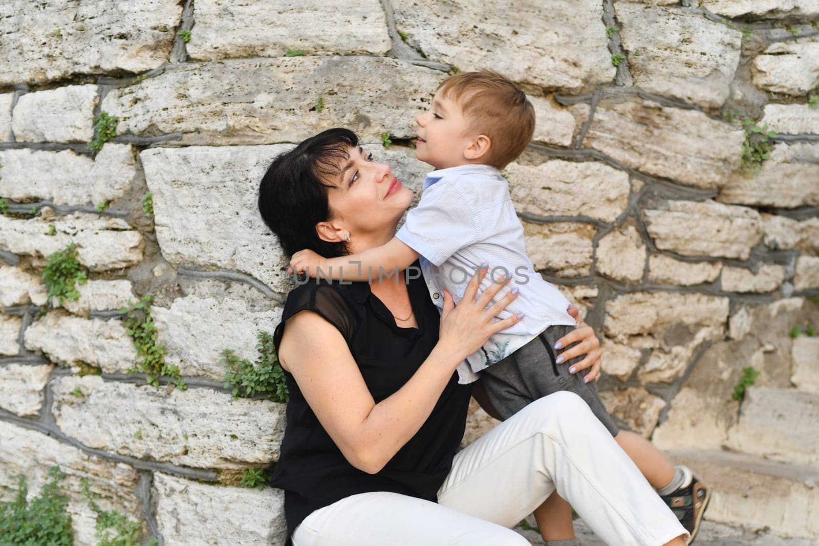 Mother hugs her son and smiles near the stone wall