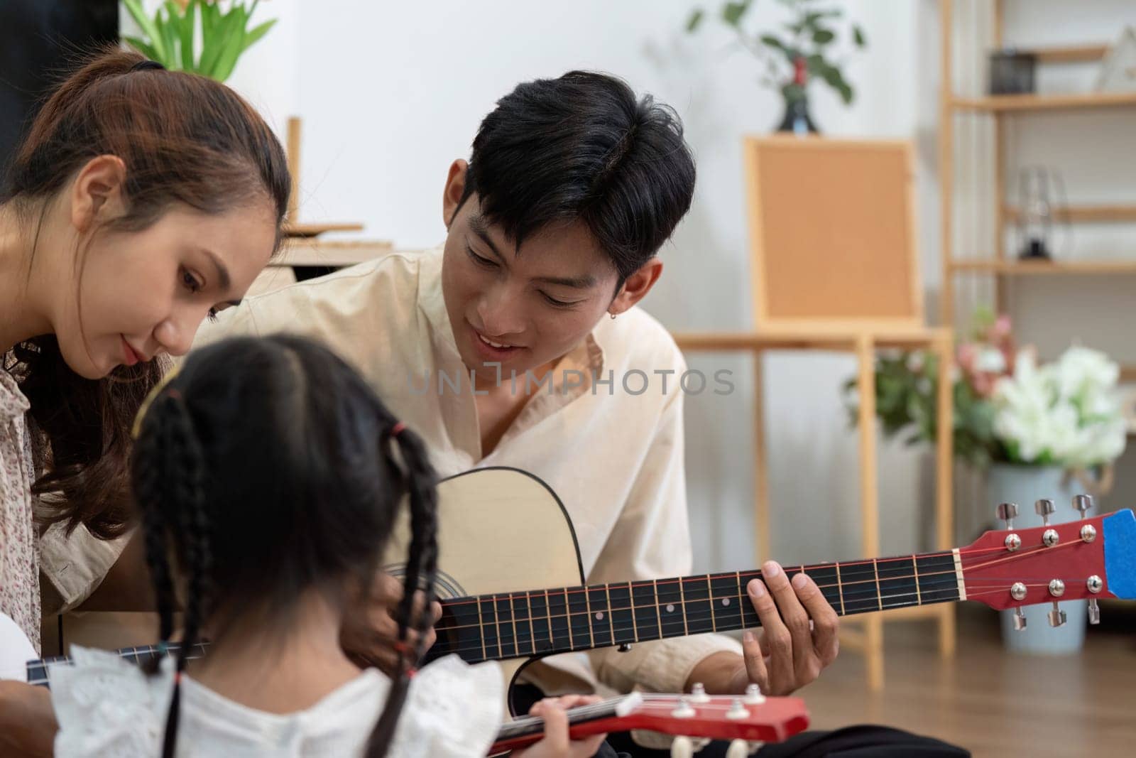 A family music session where a little girl enjoys her guitar lessons while her mother and father provide encouragement and musical collaboration.