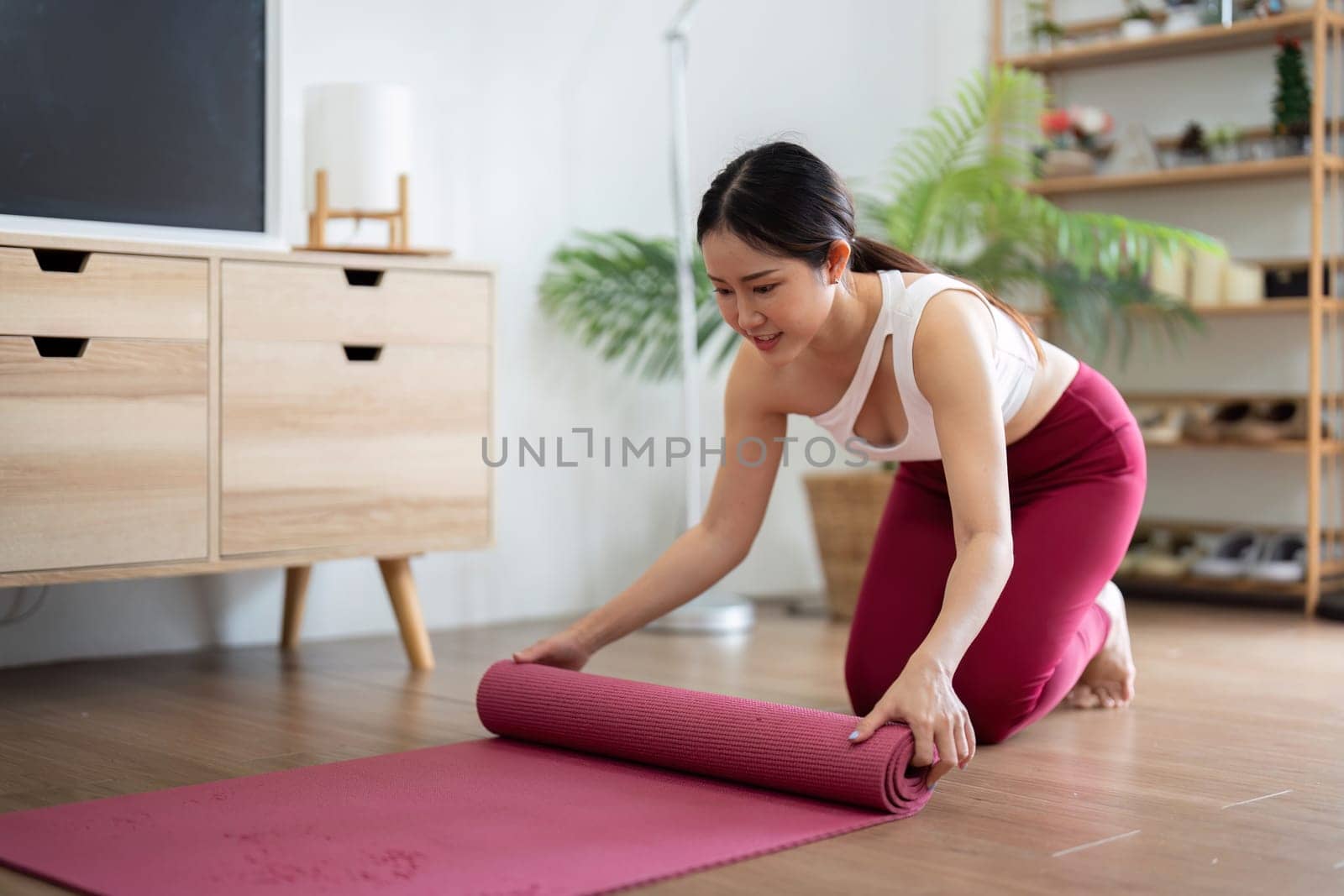 In a calm home environment, a woman rolls up her yoga mat after completing her practice, reflecting on her wellness journey and the benefits of her session.