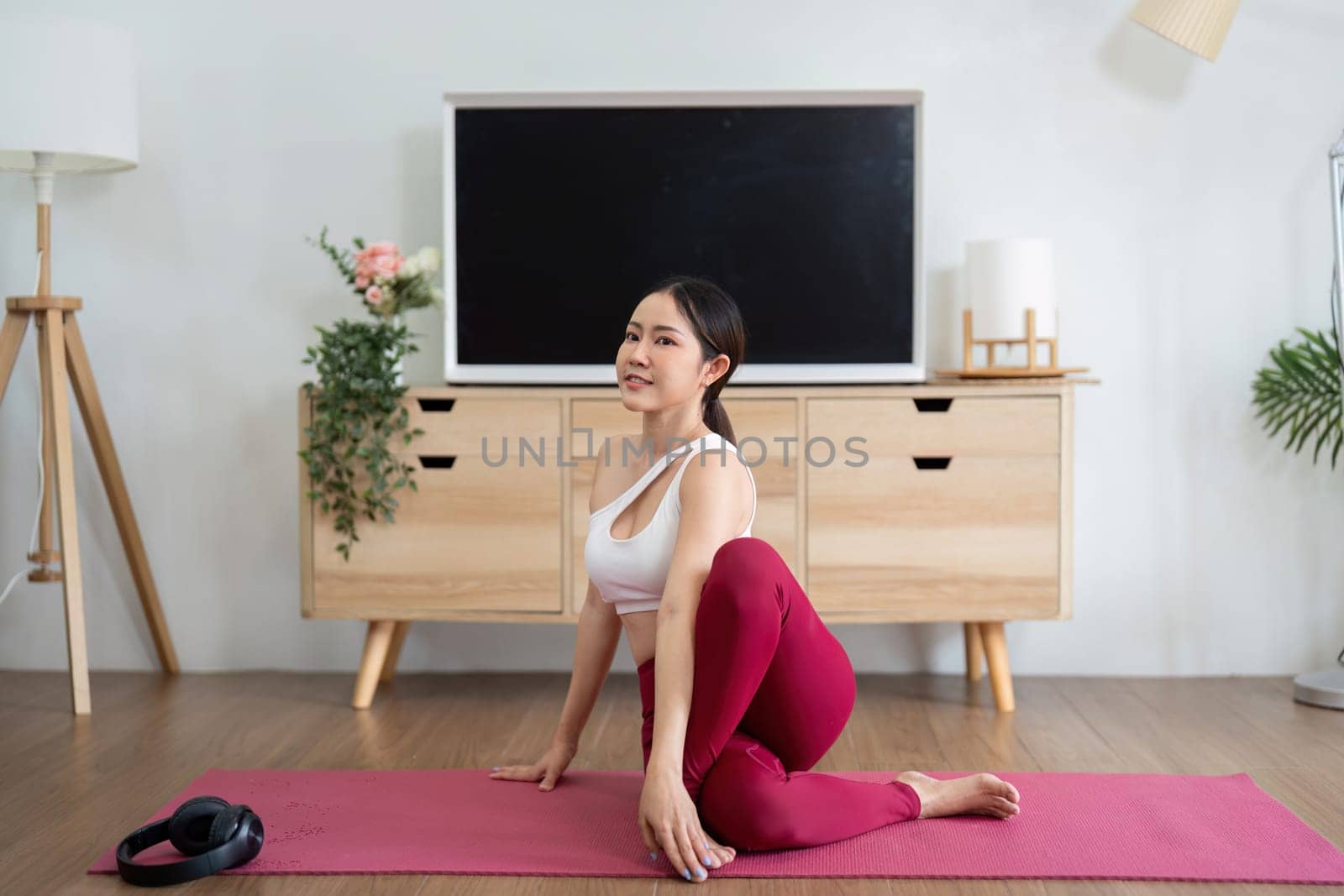 Engaged in a yoga routine, a woman performs a specific posture, emphasizing flexibility and balance in her wellness journey, in a peaceful home setting.