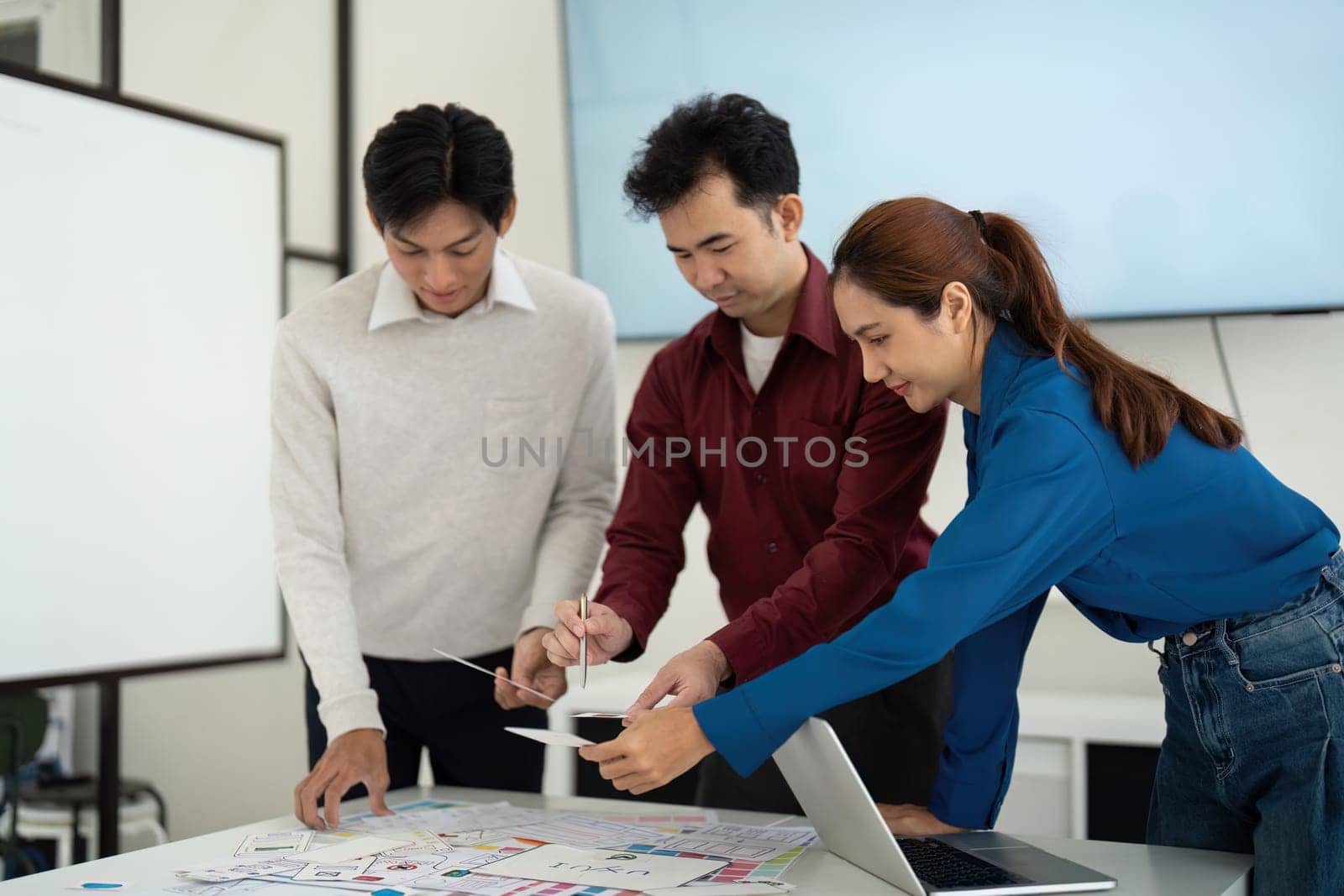 Three UX UI designers engage deeply in a collaborative discussion, refining their ideas and layouts to enhance the user experience and interface designs.