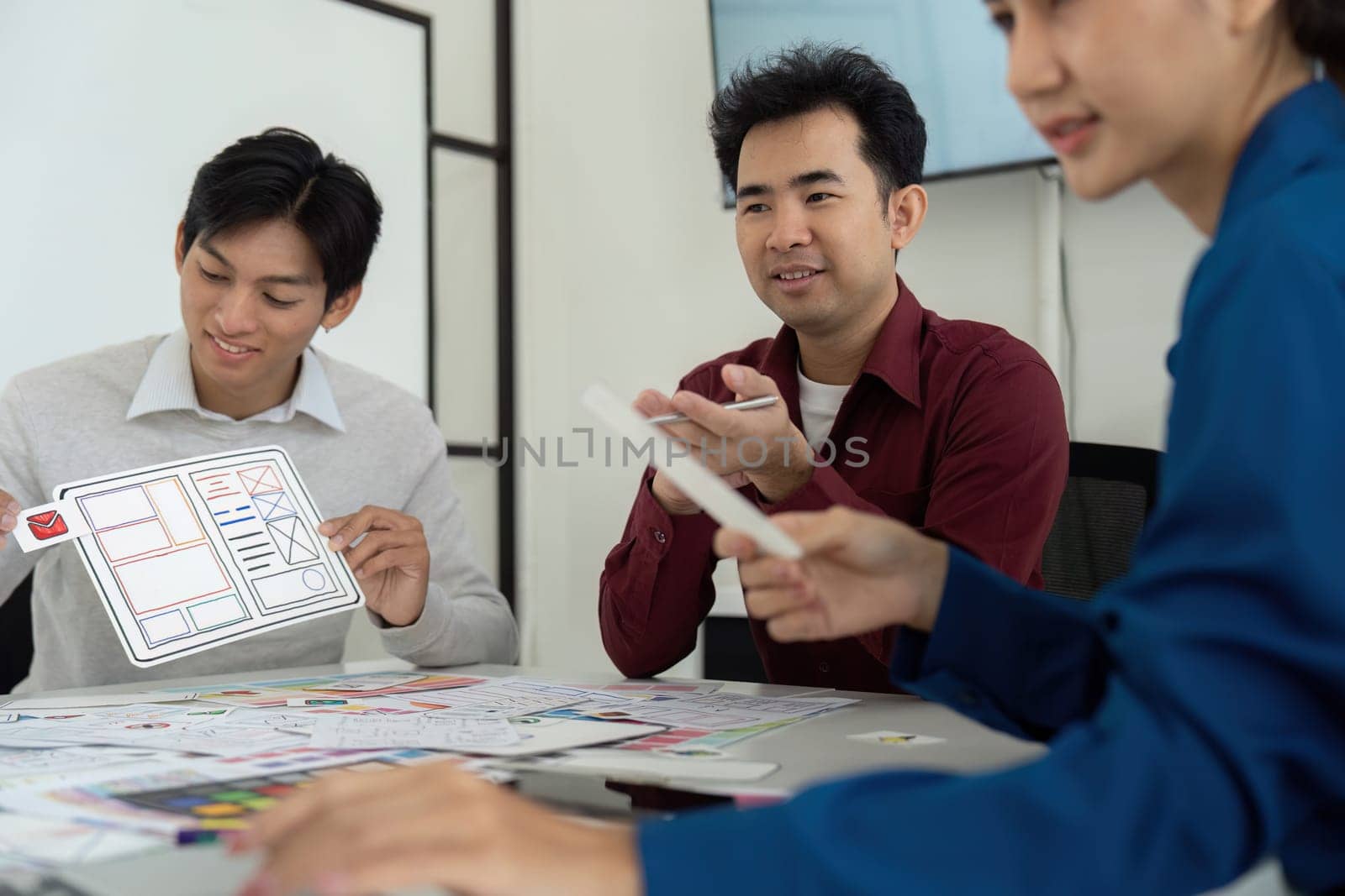 Three design experts engage in a collaborative session, discussing wireframes and user experience strategies while reviewing layout prototypes and sketches.