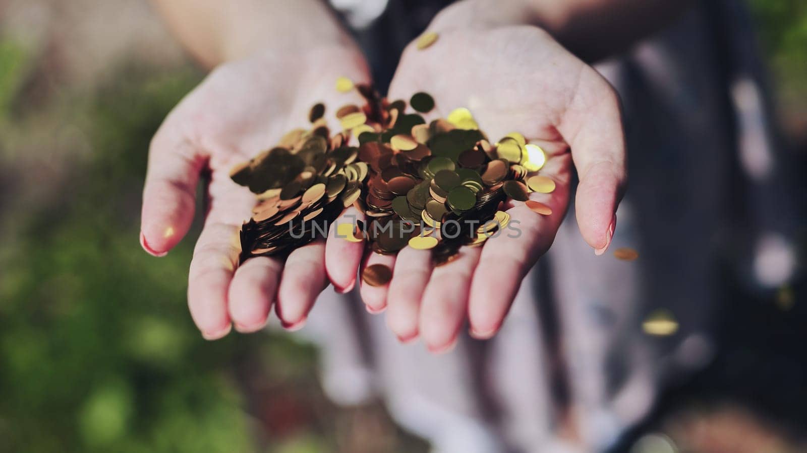 Woman is holding golden confetti in her open palms, celebrating an event outdoors in nature