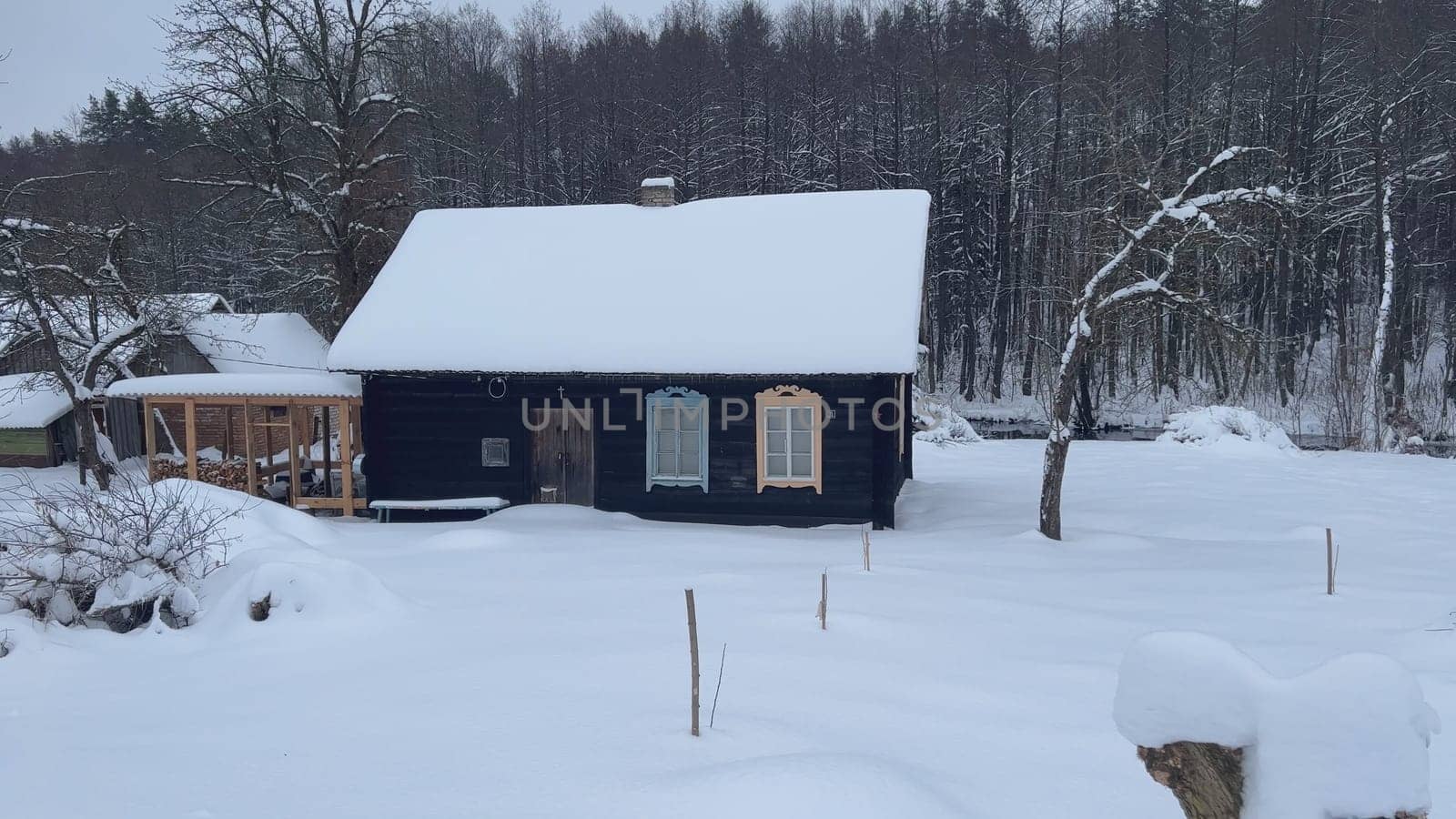 Snow covered wooden cottage with colorful window frames, located in rural Latvia during winter season