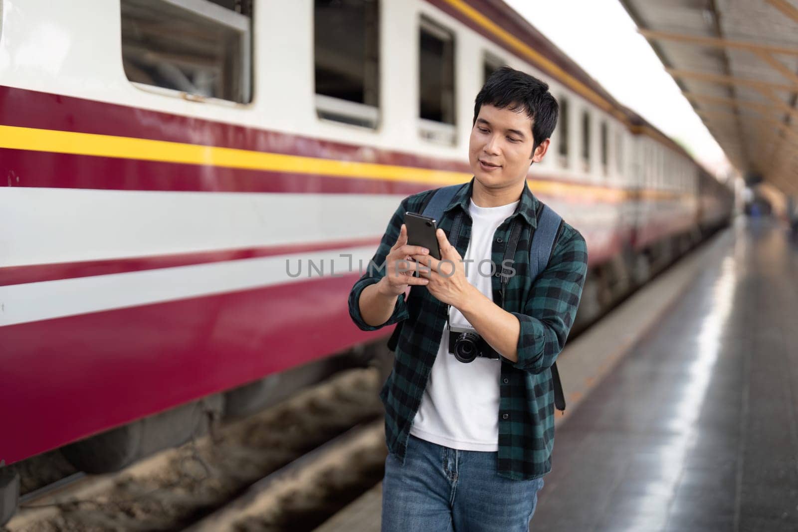 A young man stands by a colorful train platform, focusing on his smartphone, showcasing the ease of planning and connecting during travel adventures.