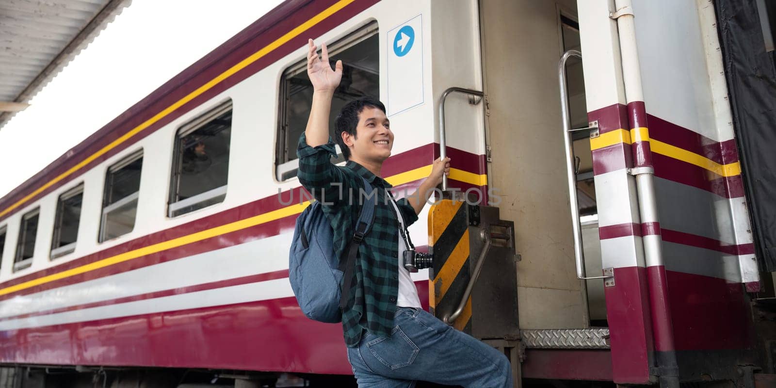 With a smile on his face, a young man climbs aboard a train, eager to begin his adventure. His backpack and camera reflect his enthusiasm for travel and exploration.