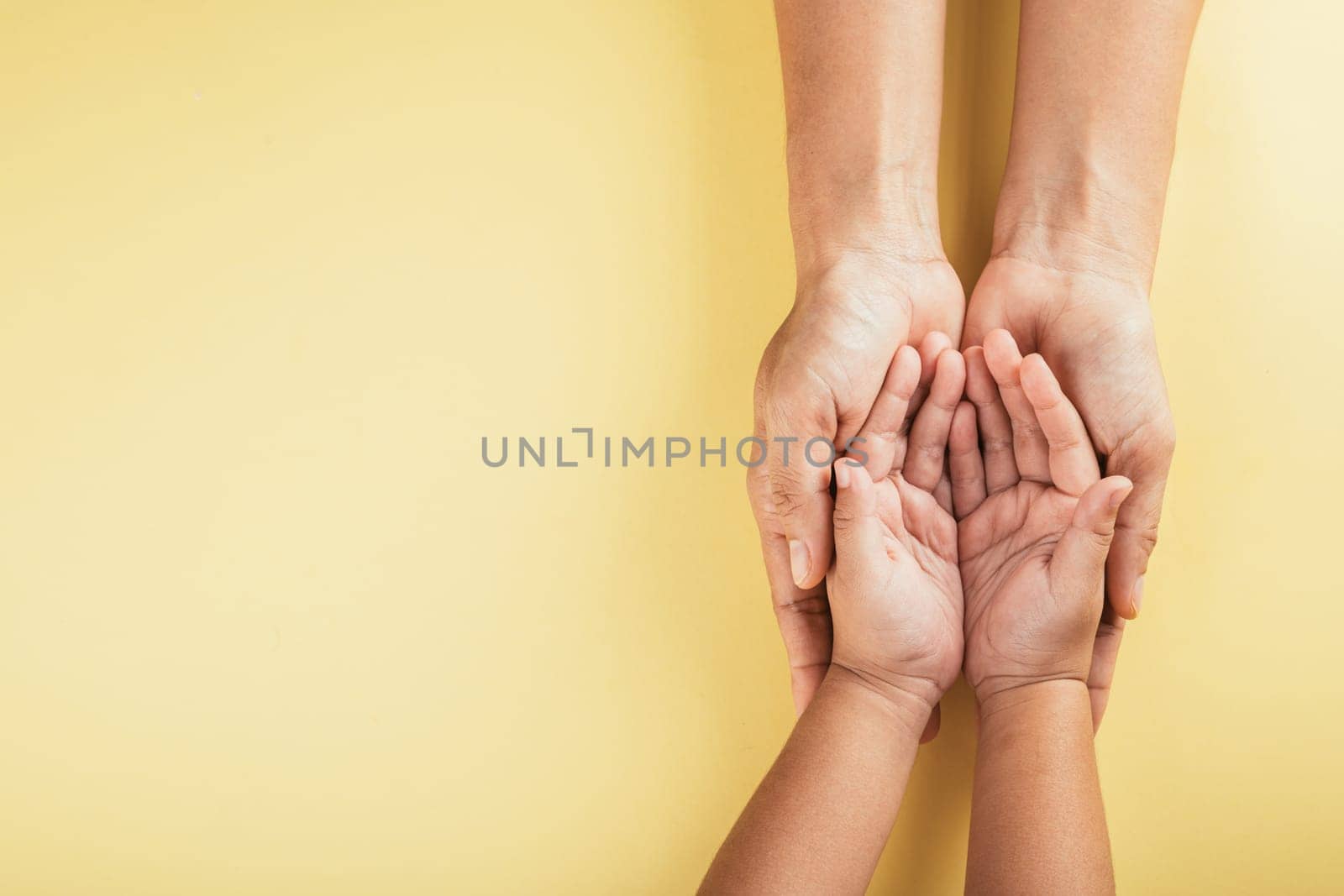 Studio shot, Close-up top view of family hands stacked isolated background. Parents and kid holding empty space together symbolizing support and love. Family and Parents Day concept.