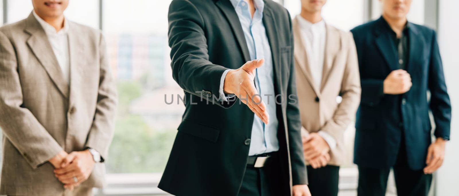 Businessman in professional suit extends his open palm in gesture of request and handshake in an office setting. This portrays the concepts of trust cooperation and successful business relationships.
