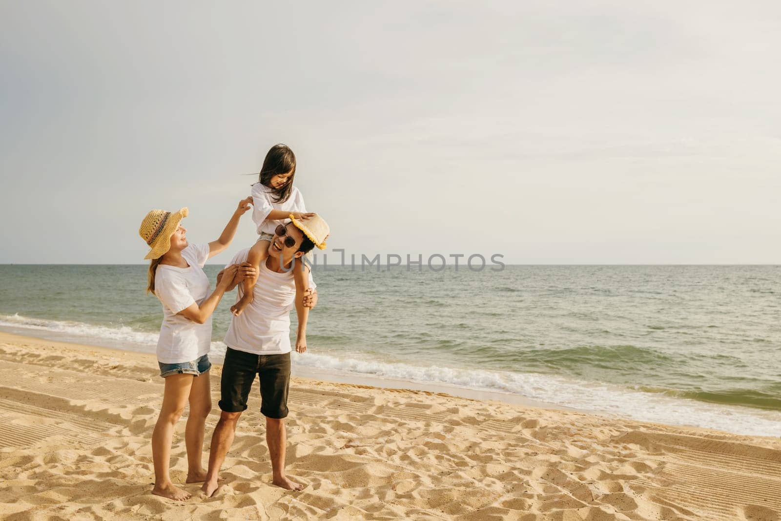 Happy family in holiday. Father, Mother and kids having fun together shoulder ride on summer beach, Parents carrying children on neck at beach, family is enjoying their summer in sunset time