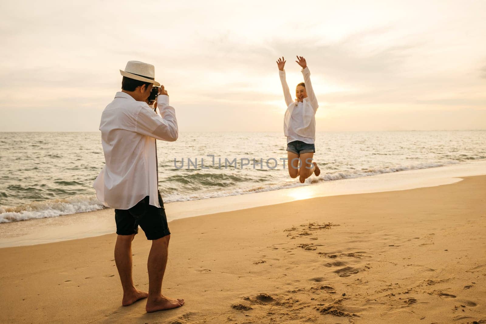 Love in focus as young couple dressed in white enjoys sunrise date on beach. boyfriend armed with camera lovingly captures snapshots of his girlfriend creating memories by ocean.
