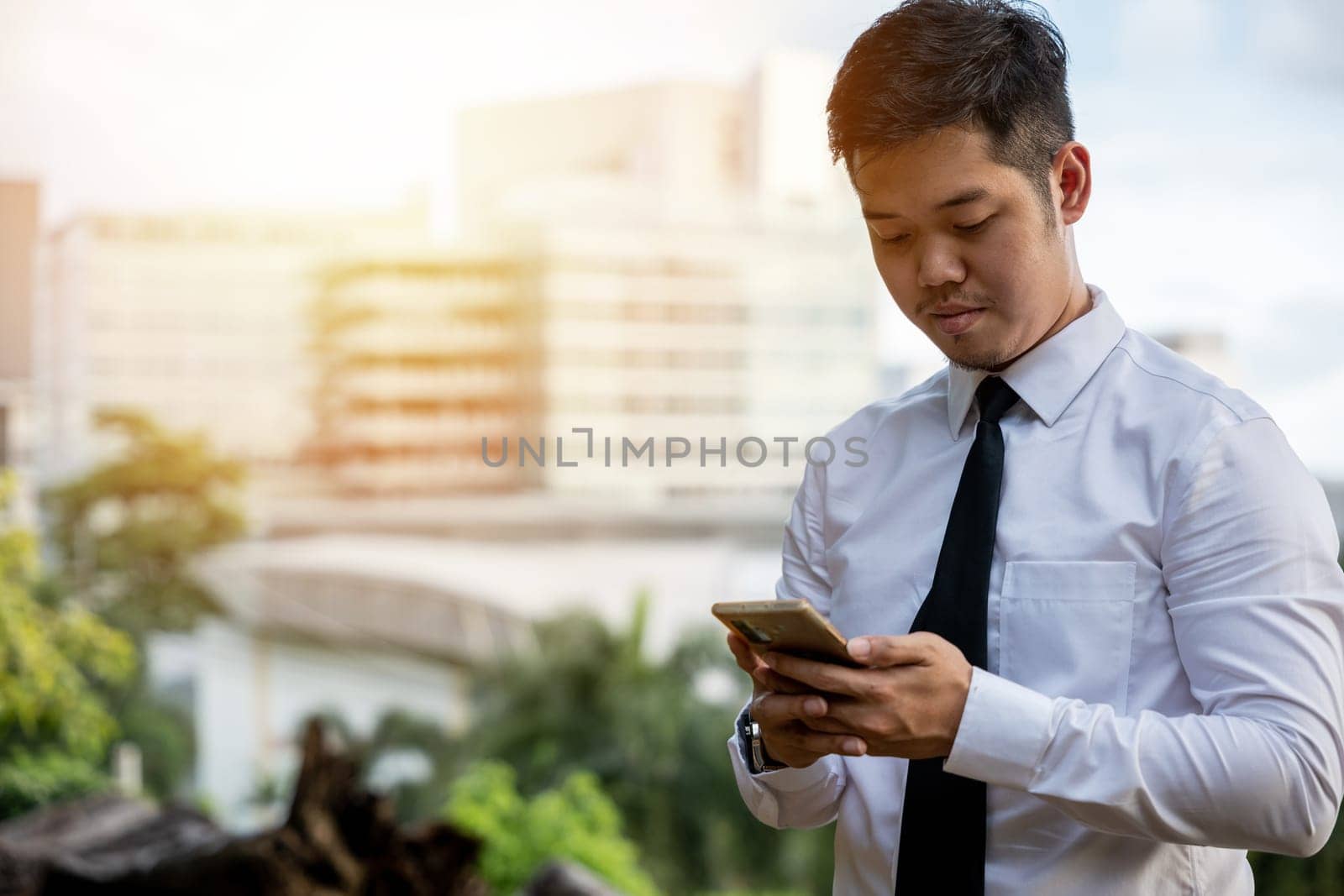 Young Asian businessman, software developer, smiles using phone app. Success in testing software outside office. Portrait of a satisfied CEO, standing, serious in technology