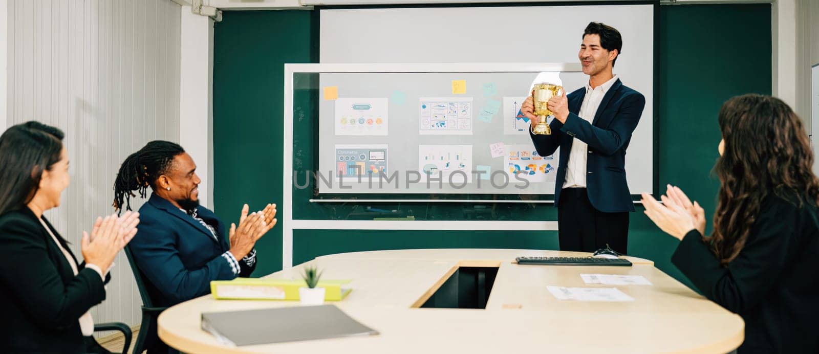 A successful businessman holds a performance trophy in a meeting room as the teamwork congratulates his achievement. This represents leadership, business success, and excellence in management.
