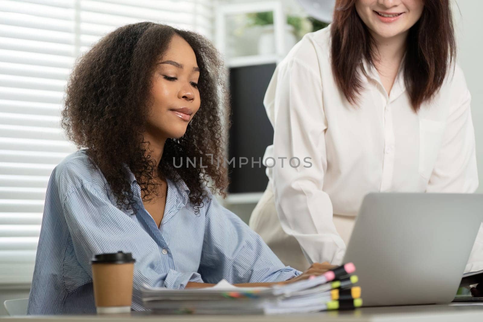 A focused work session where one colleague is dedicated to her tasks, while another provides helpful oversight, fostering a productive atmosphere.