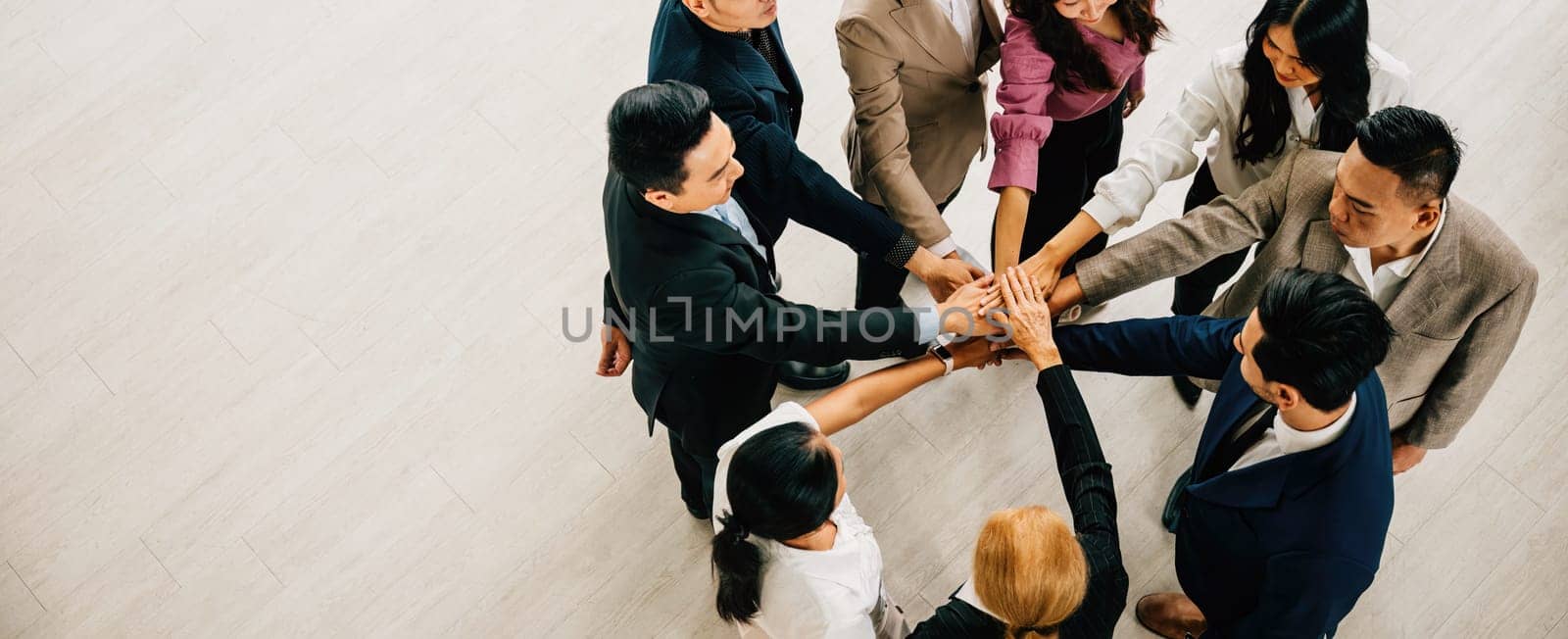 A top view captures four diverse businesspeople in a circle, hands stacked, symbolizing unity and teamwork. This image epitomizes success and global collaboration.