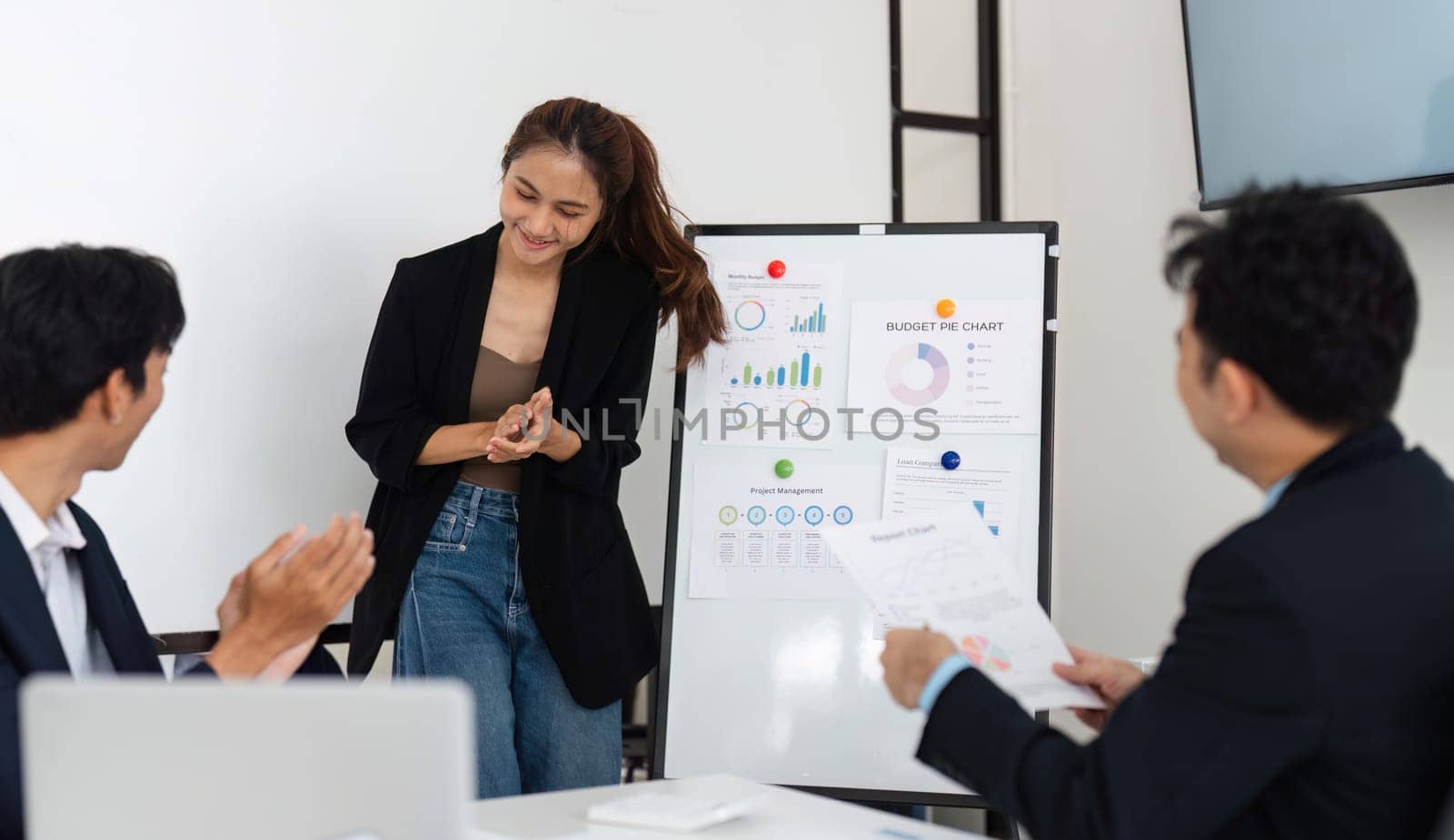 A young professional smiles as her colleagues applaud during her budget presentation, fostering a productive atmosphere of teamwork and shared goals.