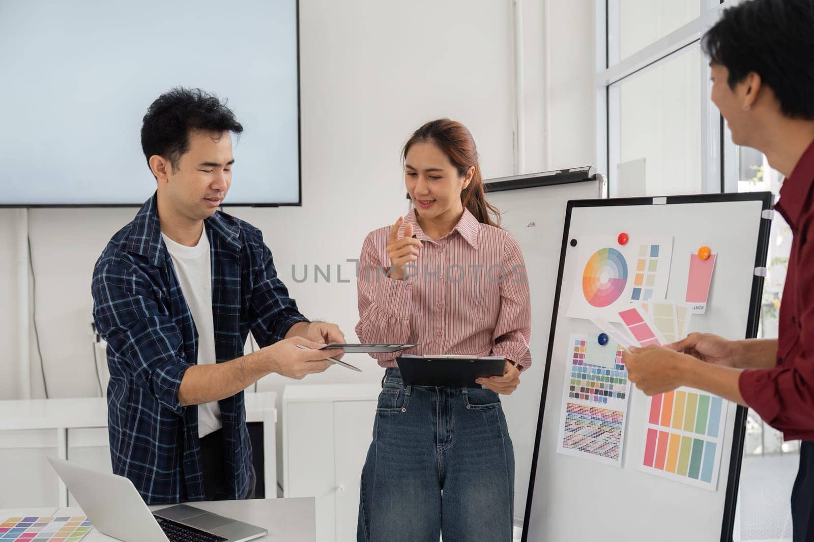 A group of creatives collaborates in a vibrant office, exchanging design ideas and feedback while examining color palettes on a tablet and board, fostering teamwork and innovation.
