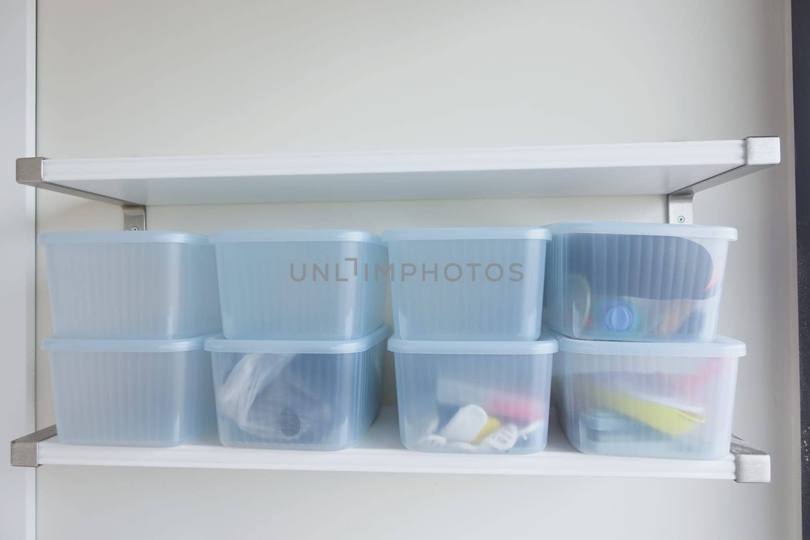 Clear storage containers arranged neatly on a white shelf in a clean area.