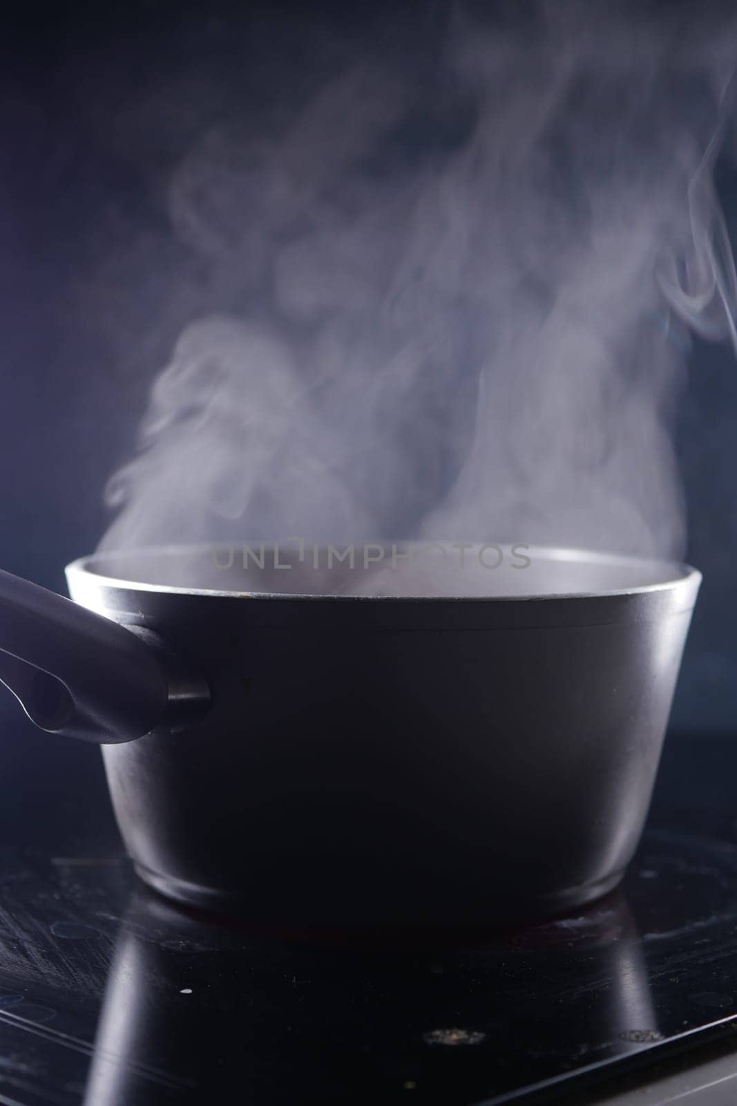 Steam rises from a pot placed on a reflective kitchen surface in low light.