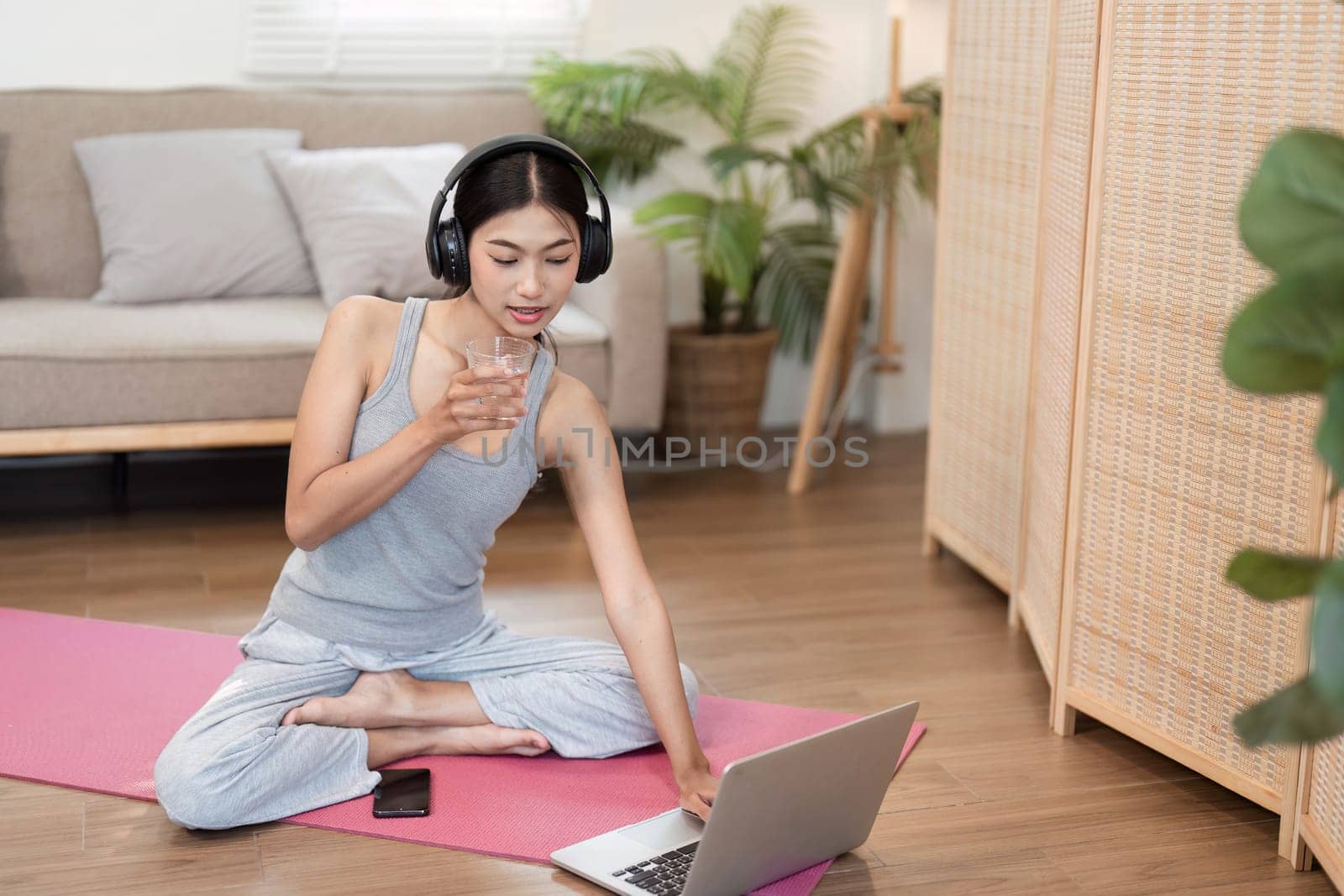A dedicated yogi engages in yoga practice at home, sipping water while discovering her inner peace through mindfulness and relaxation.