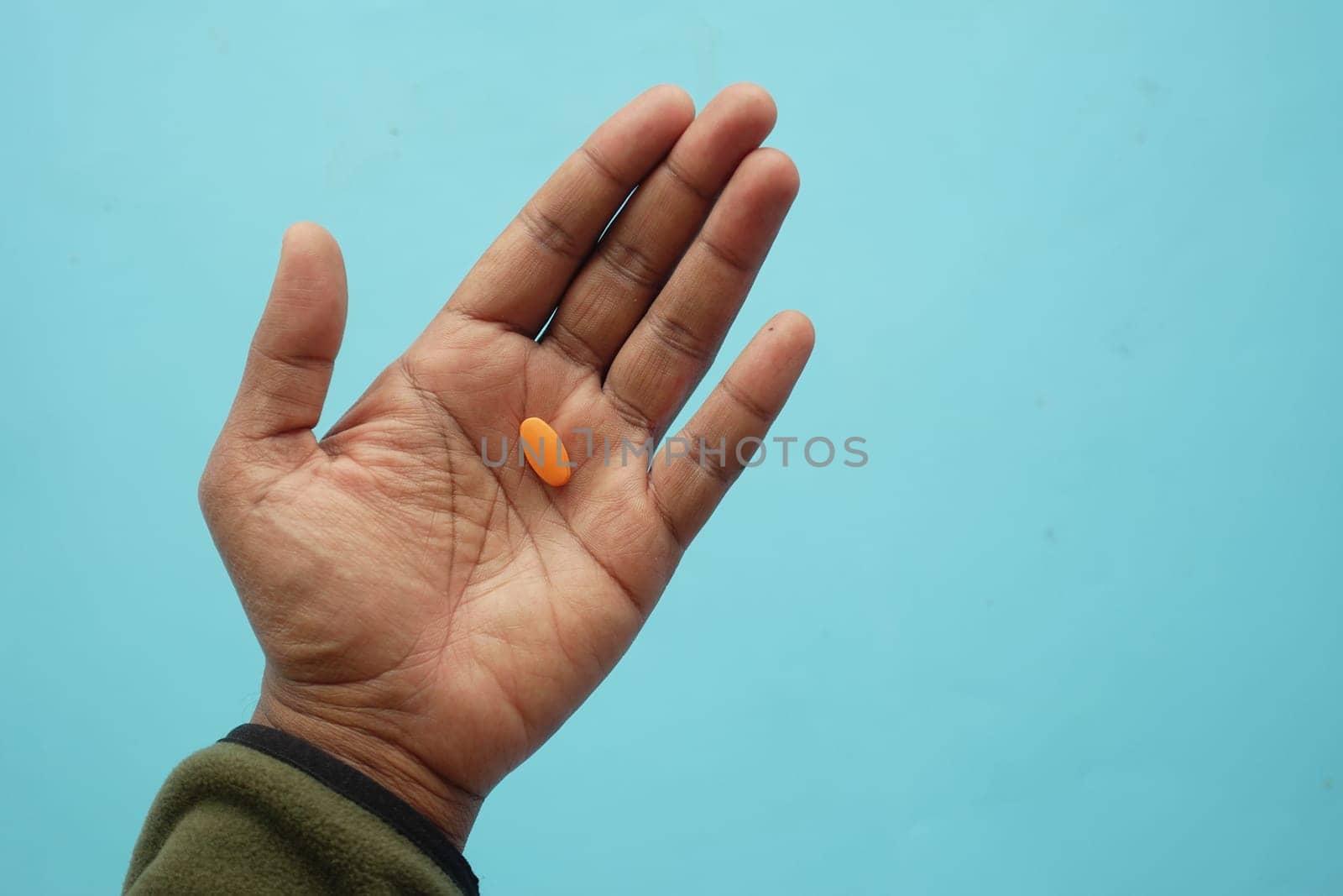 A hand with an orange tablet resting on the palm, set against blue.