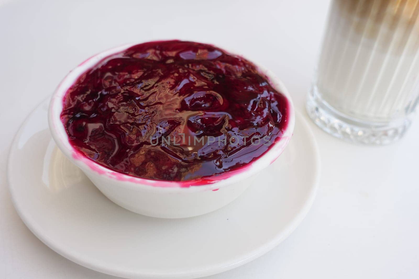Fresh berry compote in a bowl beside a glass of creamy beverage.