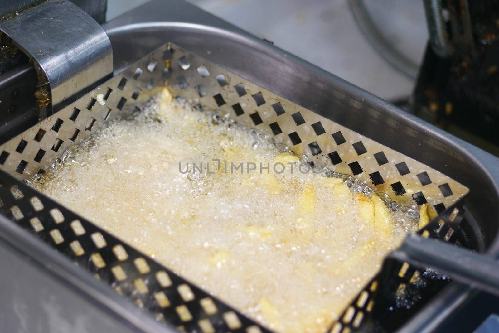 Golden fries bubbling in hot oil within a deep fryer basket.