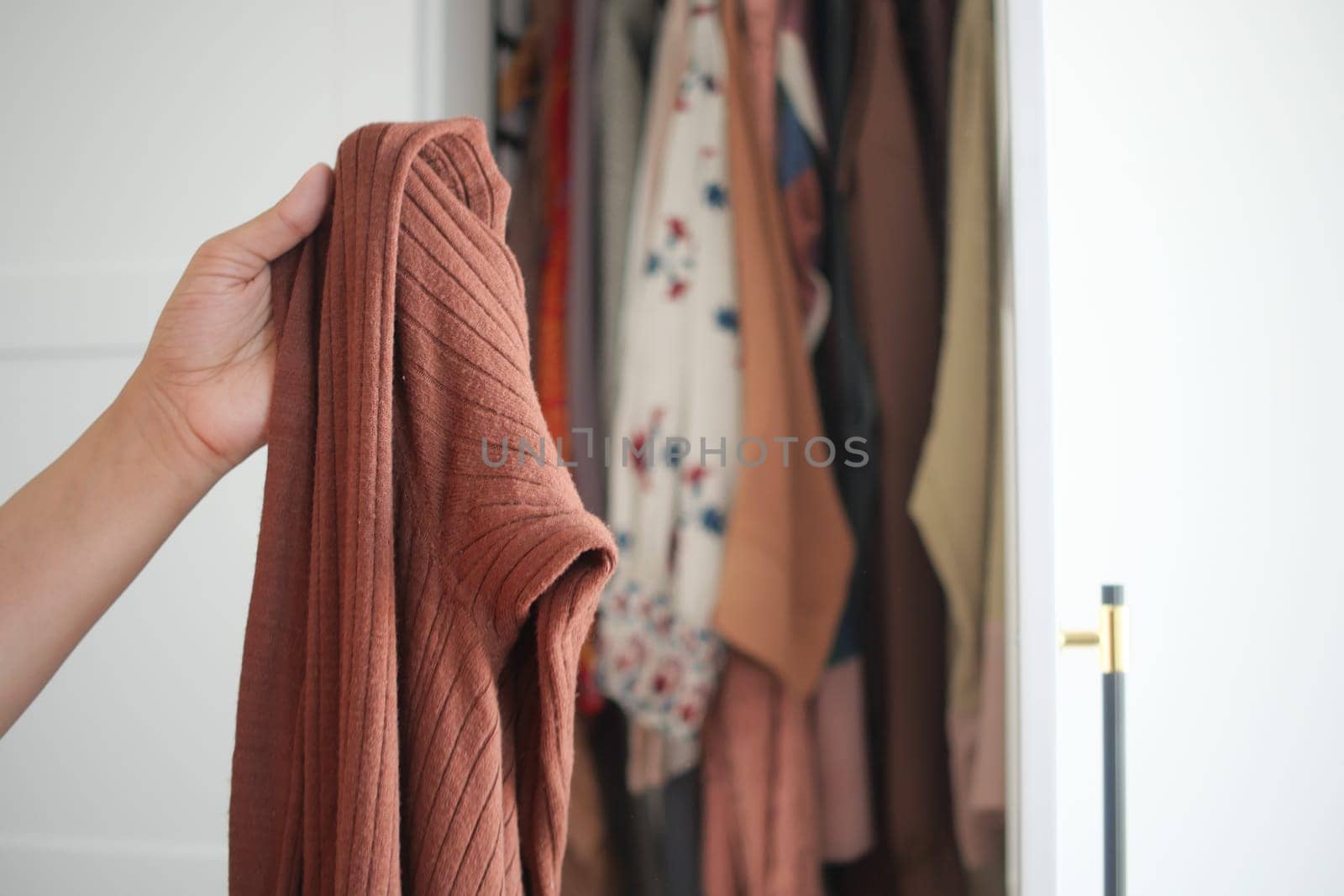 A person holds a textured brown piece of clothing while standing near a closet.