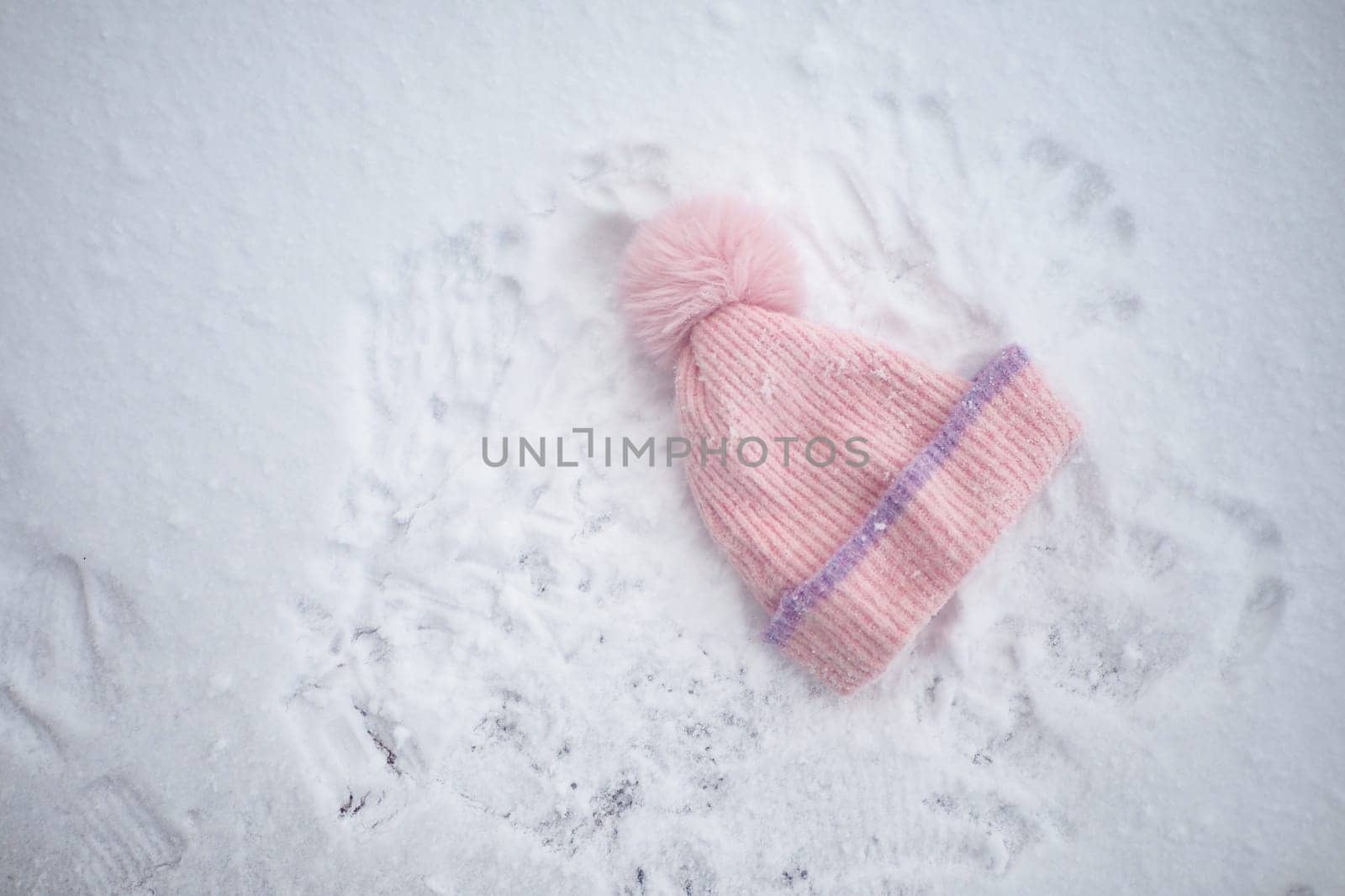 A soft pink hat lies in the snow surrounded by playful handprints.