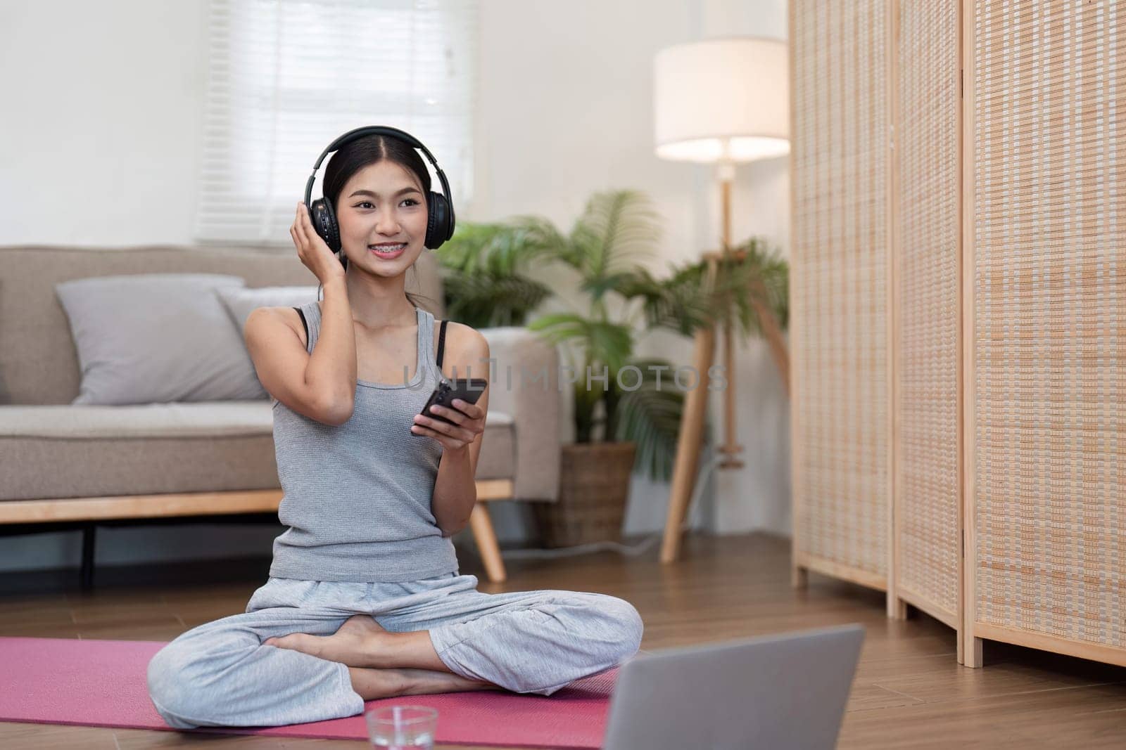 A happy woman sits cross-legged on a yoga mat, connecting with others through her phone while enjoying a peaceful moment.