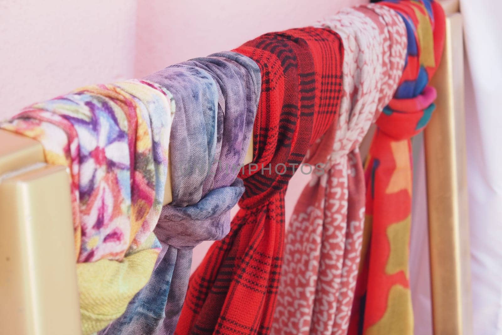 Various colorful scarves are displayed on a clothes rack indoors.