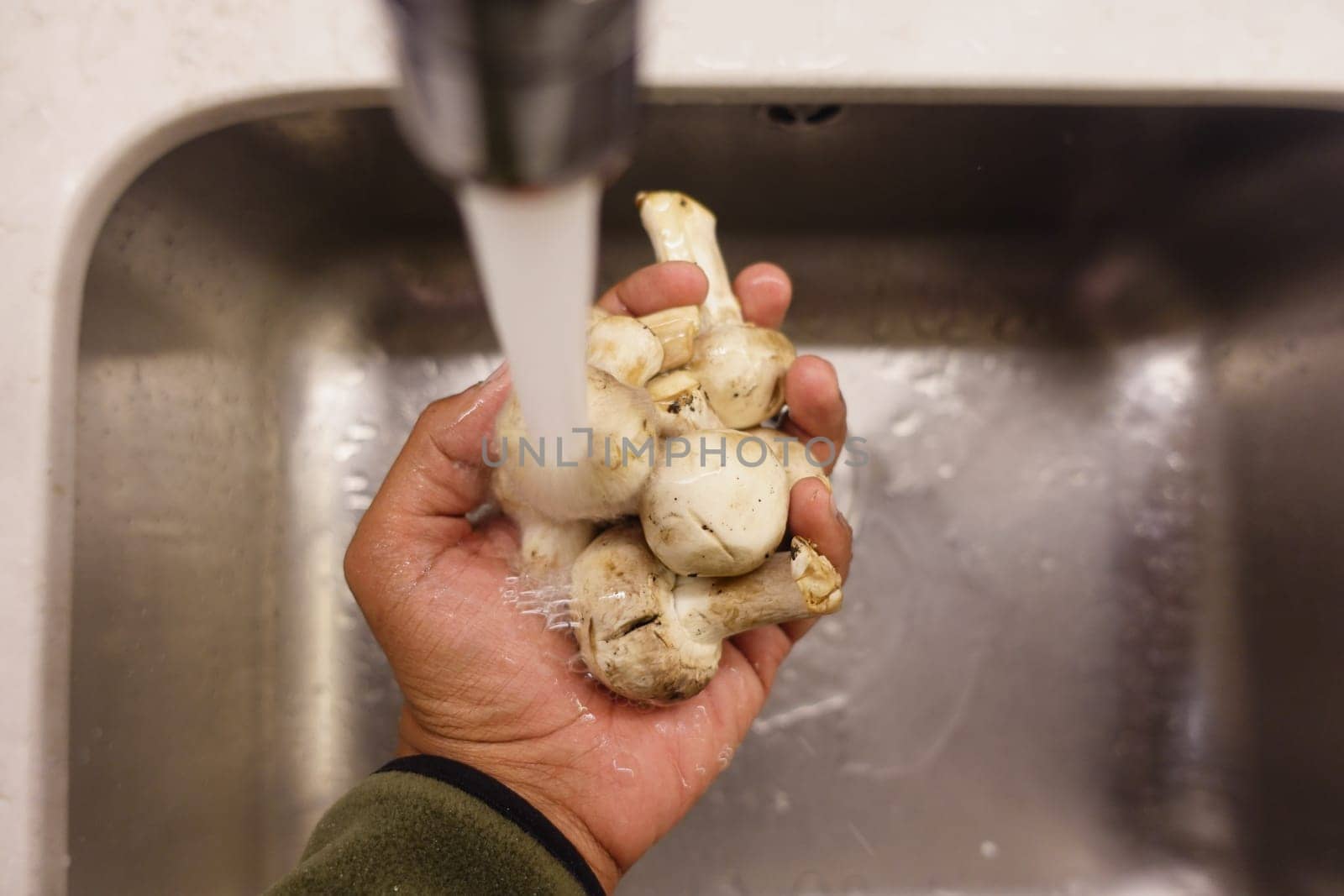 A hand holds mushrooms while they are rinsed under cold water.