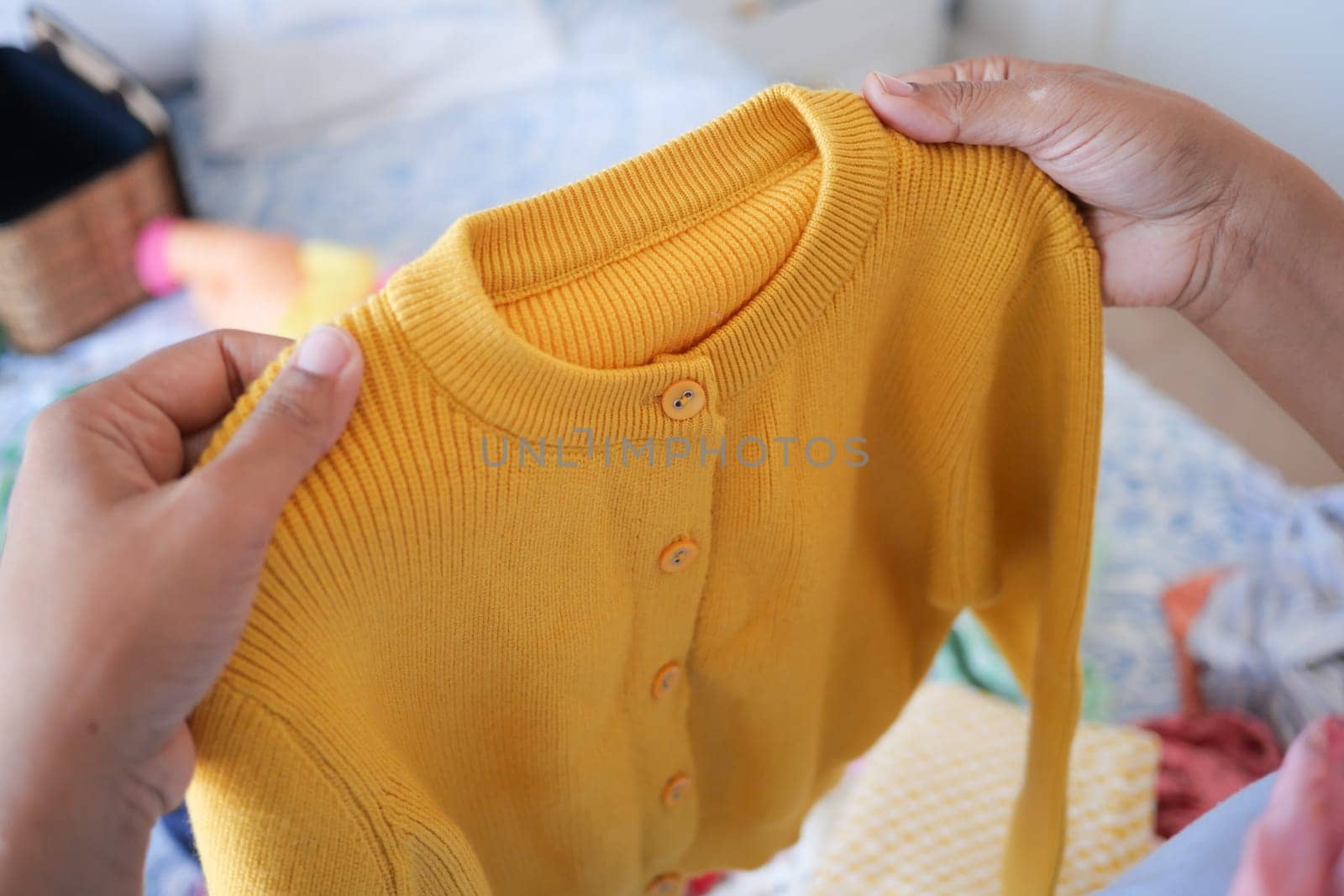 Hands grasp a yellow cardigan amid a colorful assortment of clothing.