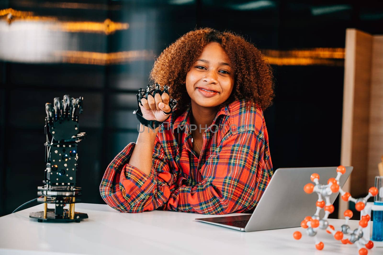 In a classroom a Black teenage student tests a robotic arm delving into subjects of interest. Embracing innovation and technology for skill development and joyful learning.
