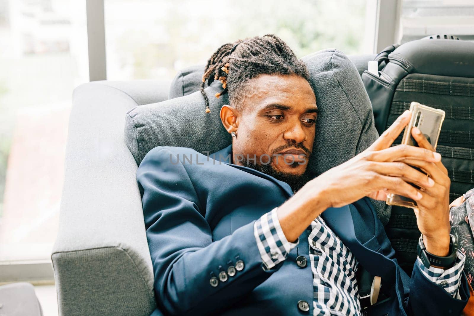 A happy and handsome black business man relaxes on a comfortable sofa in his cozy living room, joyfully using his smartphone for social networking, messaging, and online content browsing. relax time