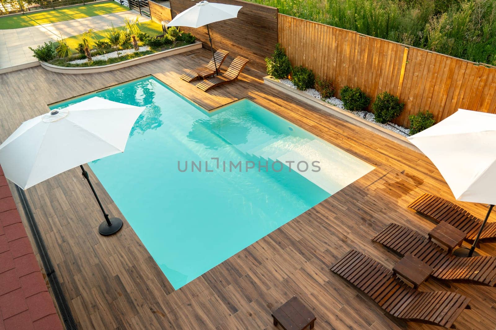Stylish backyard with turquoise swimming pool, wooden deck, lounge chairs, and white umbrellas