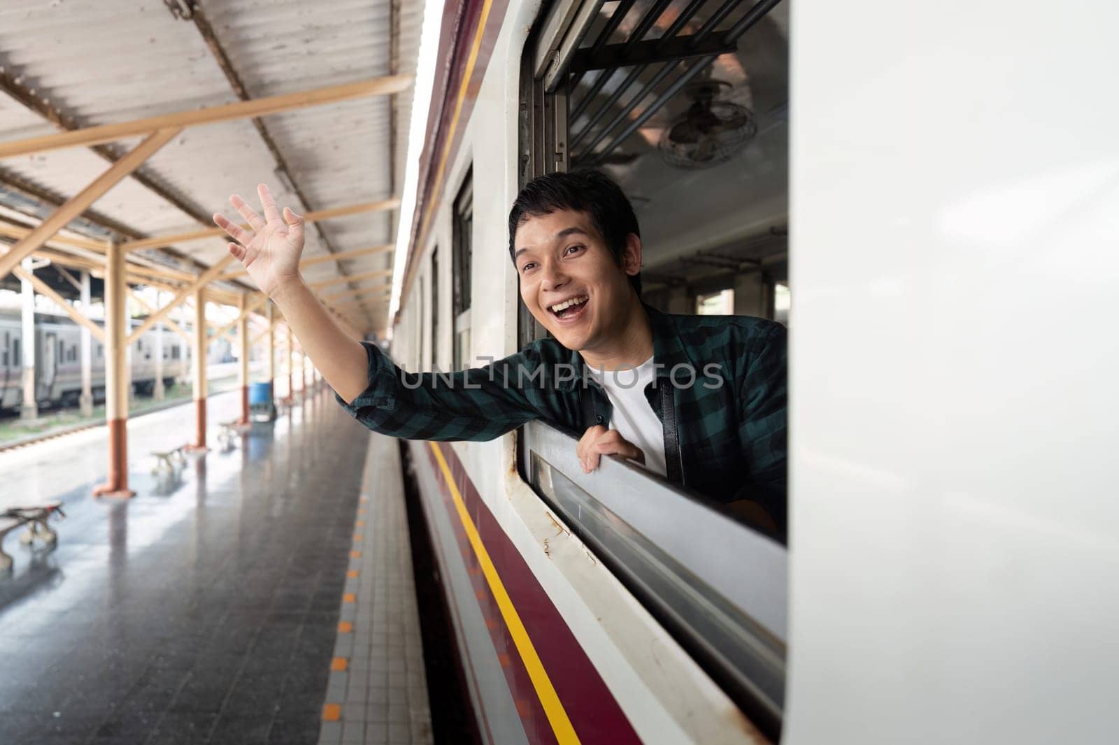 A cheerful young man waves goodbye from the train window, excited for the adventures that lie ahead of him on his journey.