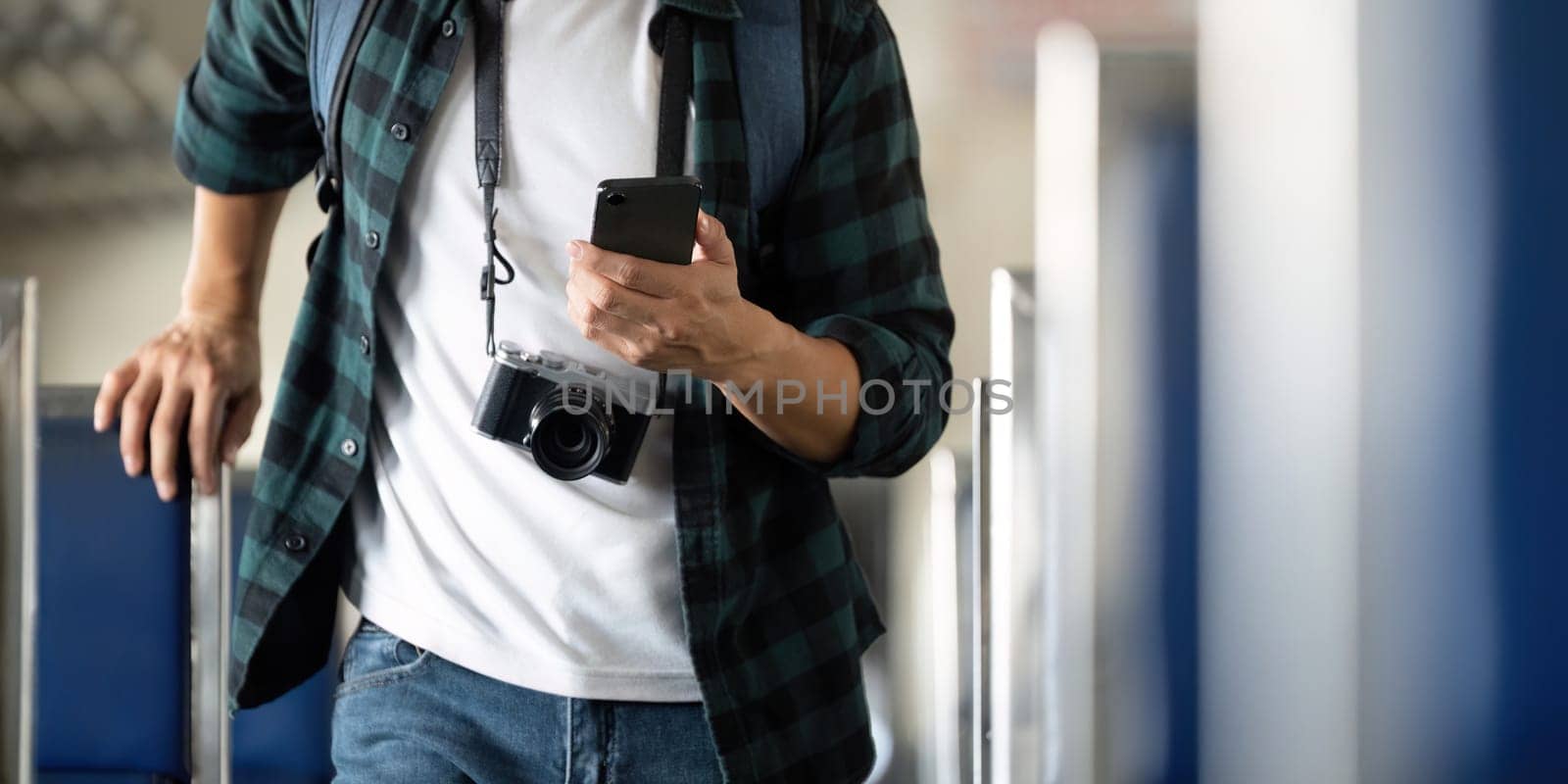 Capturing moments during his journey, a young man with a camera leans against a train seat, checking his phone for updates on his travels.