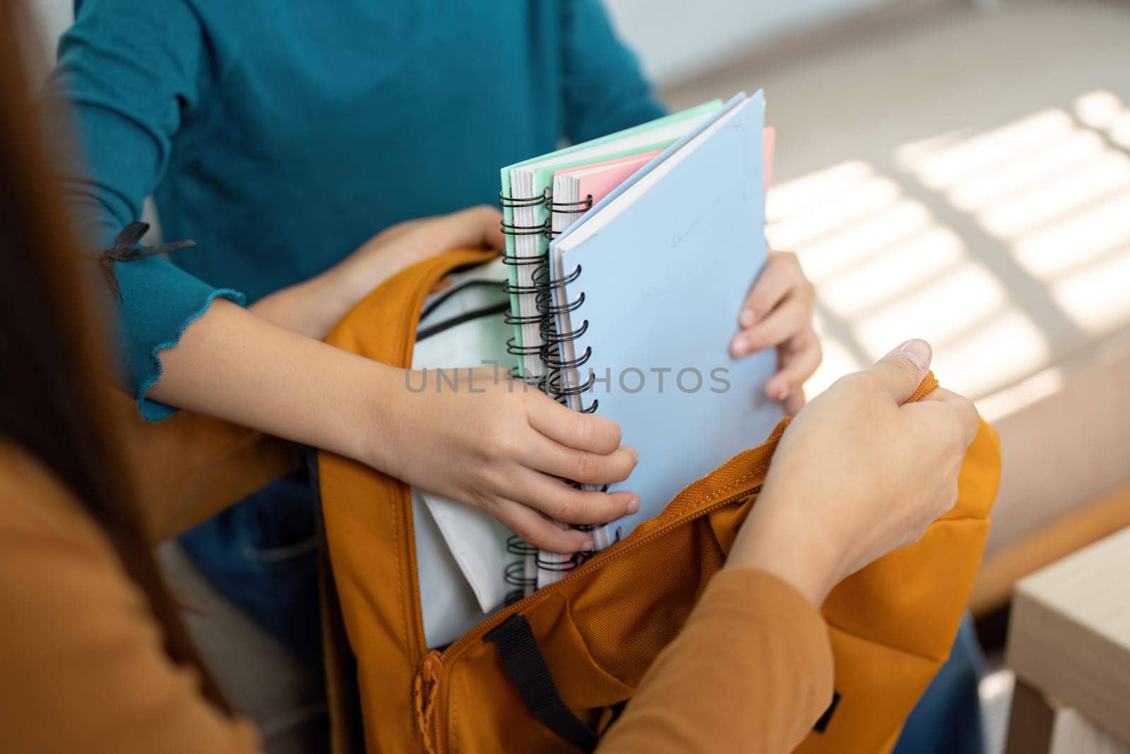 A mother assists her daughter in packing essential school supplies into a bright orange backpack, highlighting the importance of organization and preparation for school.