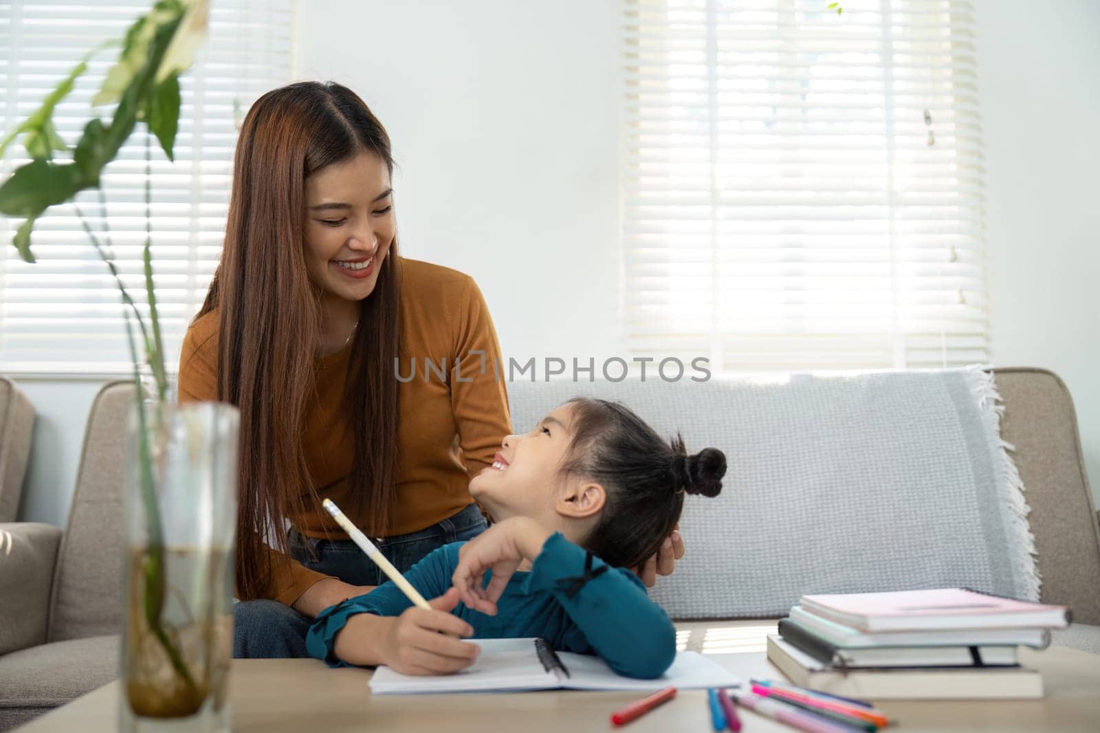 A mother engages with her daughter during homework, fostering a nurturing atmosphere while they share smiles and learning.