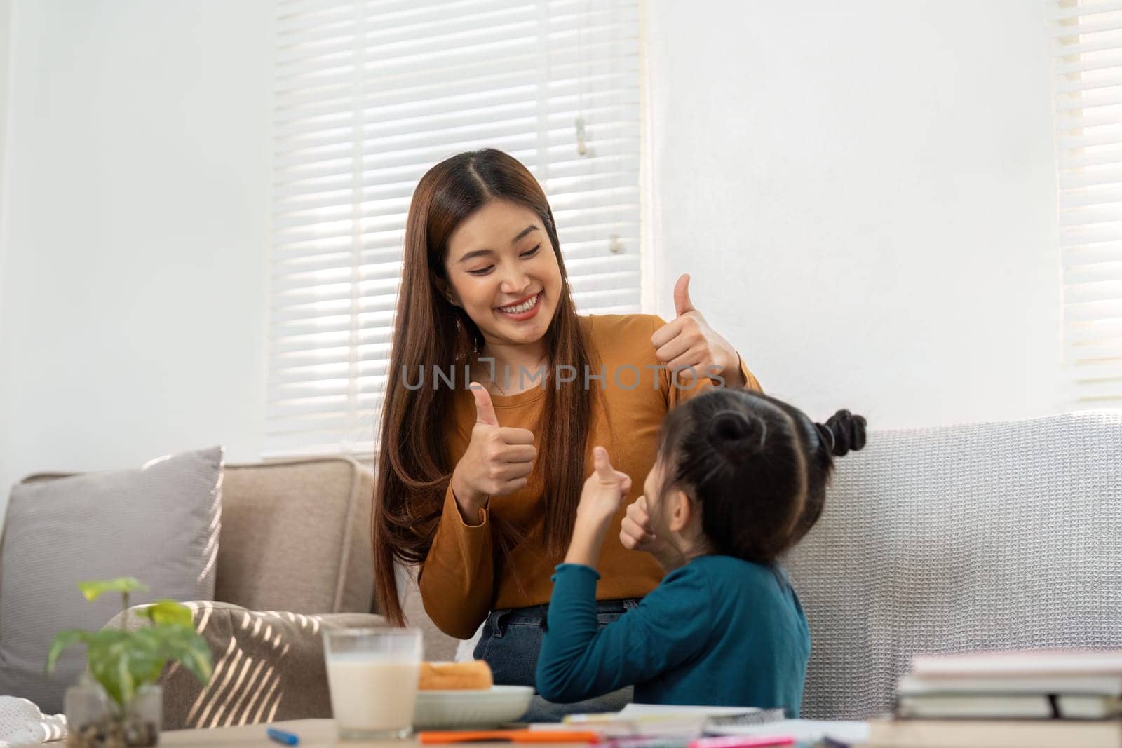 A mother and daughter share a fun moment, giving thumbs up, celebrating the joy of learning and achievements together.