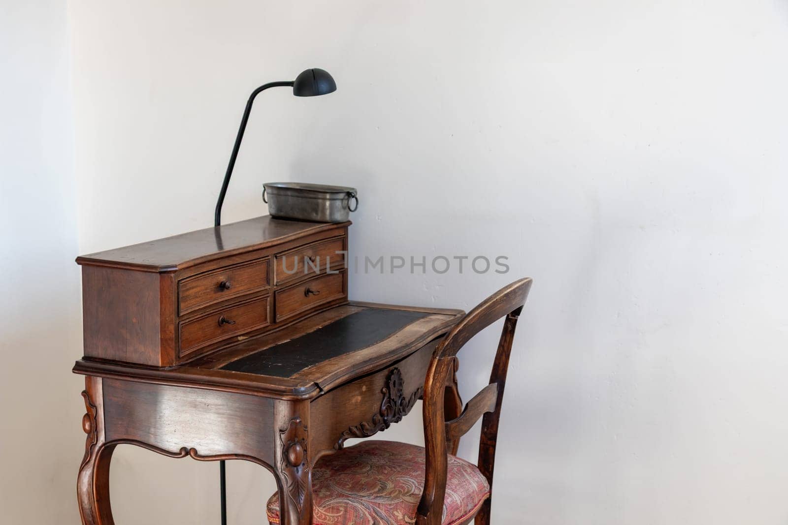 An old vintage brown work desk, wooden table with small drawers and a antique chair at home, white wall as a background with a copy space