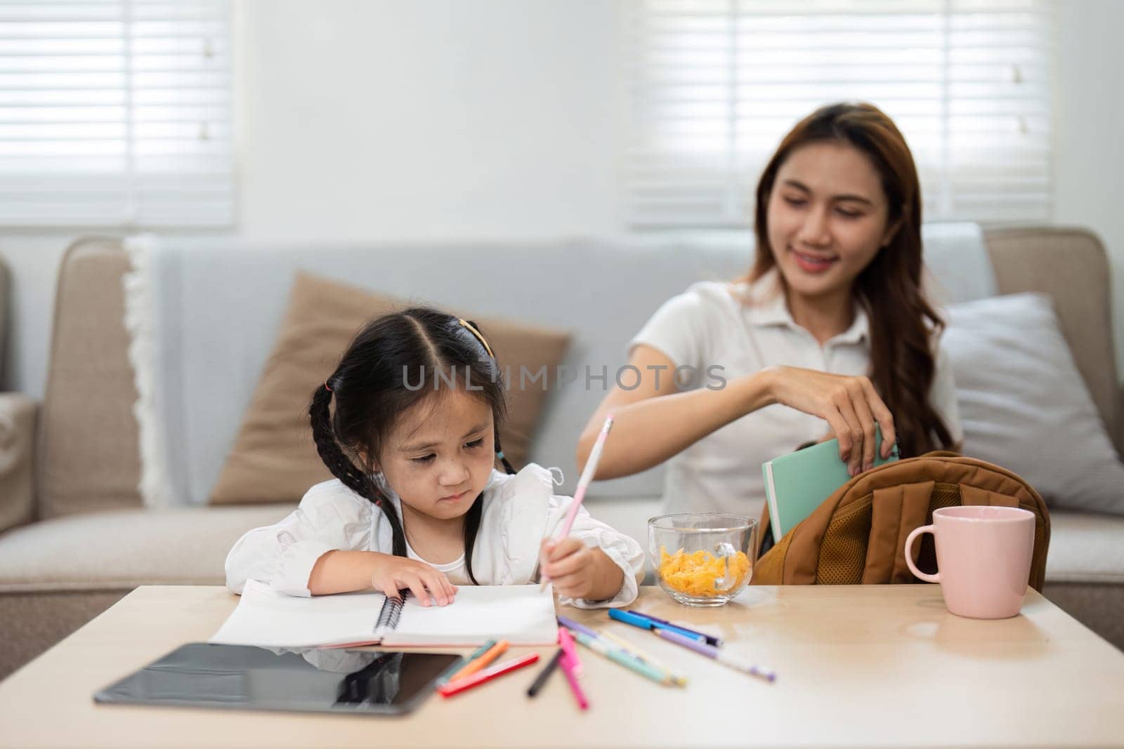 A loving mother watches her daughter as she draws, highlighting the joy of preparing for back to school, and spending quality time together.