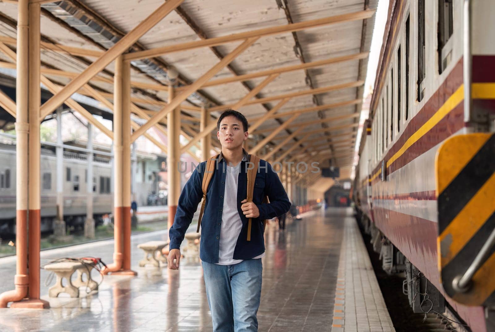 A focused young man strides through the train station, eager to catch his train. His backpack signifies travel and exploration.