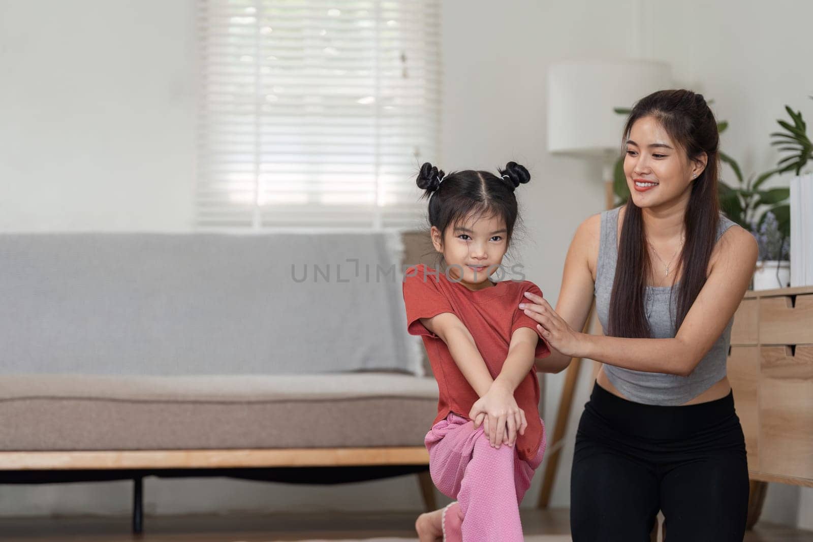 In a serene home setting, a mother provides support and instruction to her daughter, helping her master new yoga techniques while enjoying quality time together.