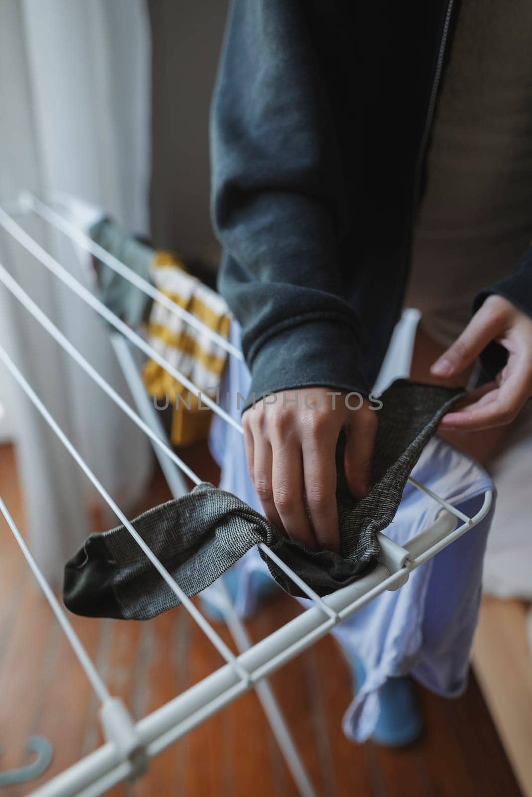 In a cozy indoor environment, a person carefully organizes and arranges black pants on a drying rack