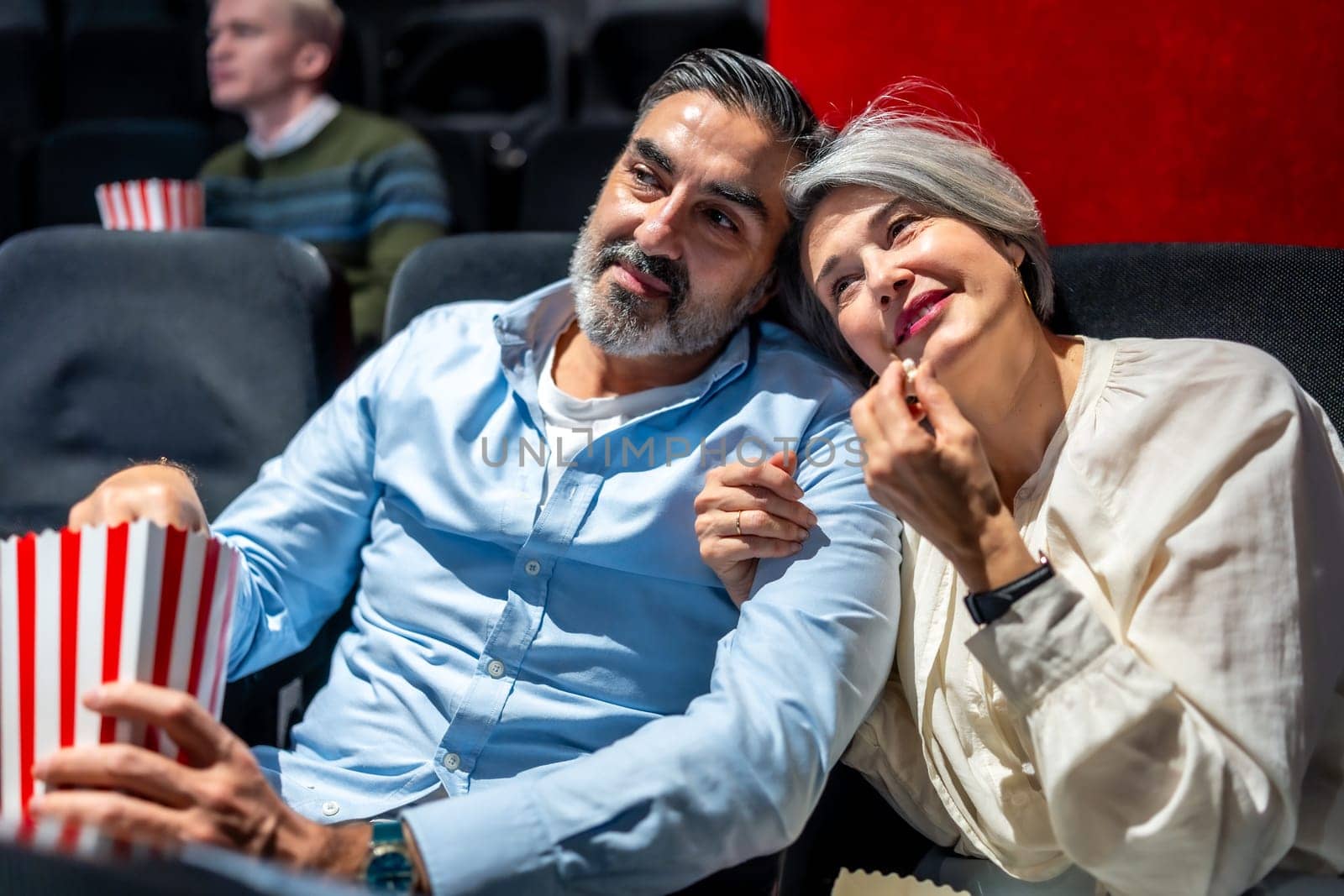 Senior couple enjoying a cozy movie night at the cinema, savoring popcorn while sharing a heartfelt moment filled with joy and affection