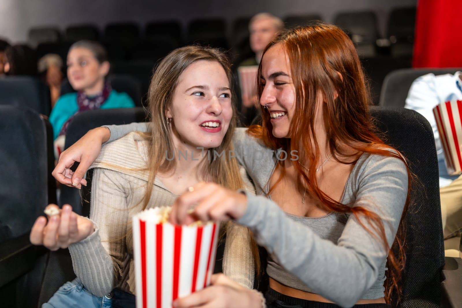 Two female friends enjoying a movie night, sharing popcorn and laughs, creating a joyful and memorable cinema experience