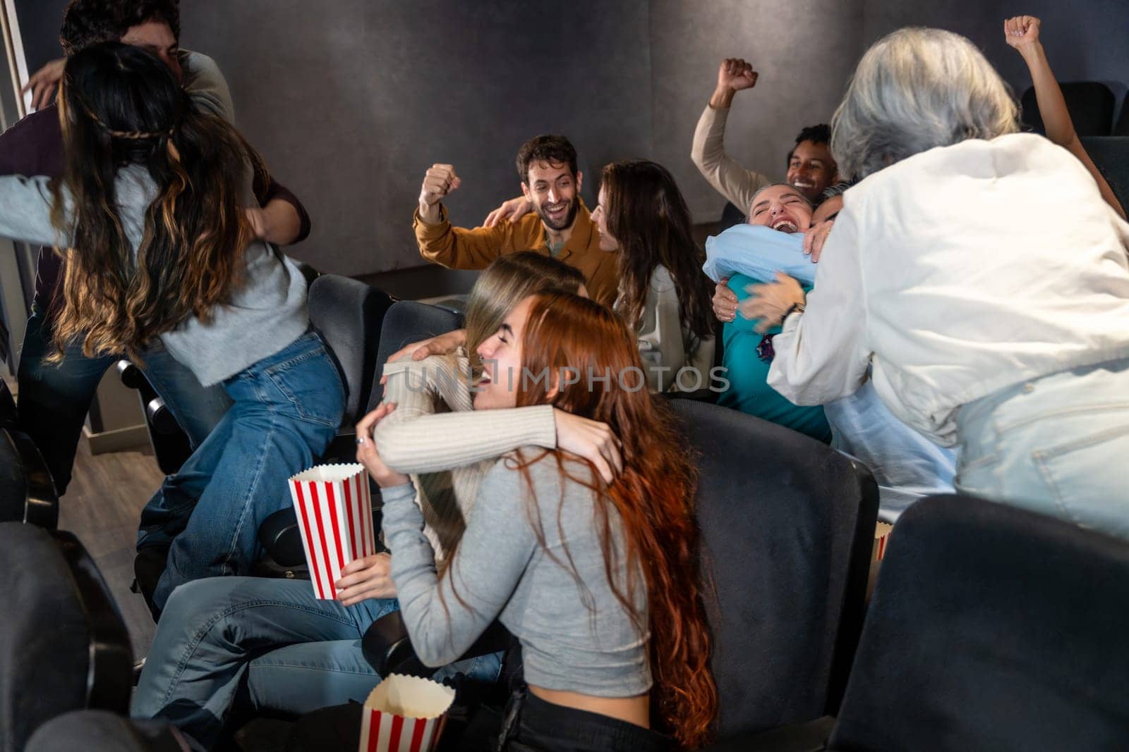 Enthusiastic friends are enjoying a movie at the cinema, hugging, cheering, and sharing a joyful moment together