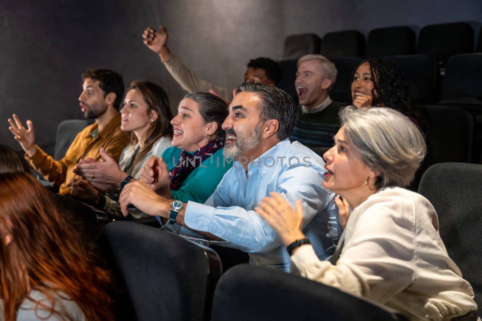 Enthusiastic moviegoers of diverse ages are cheering and applauding, fully engaged in the movie experience